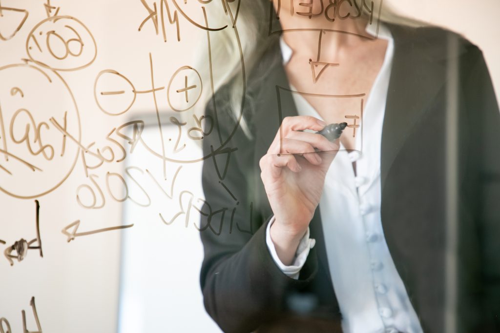 Unrecognizable grey-haired businesswoman writing on glass board