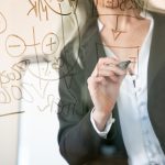 Unrecognizable grey-haired businesswoman writing on glass board