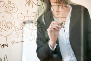 Unrecognizable grey-haired businesswoman writing on glass board