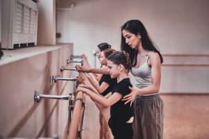 Expirienced ballet teacher is showing to young girls how to do important exercises
